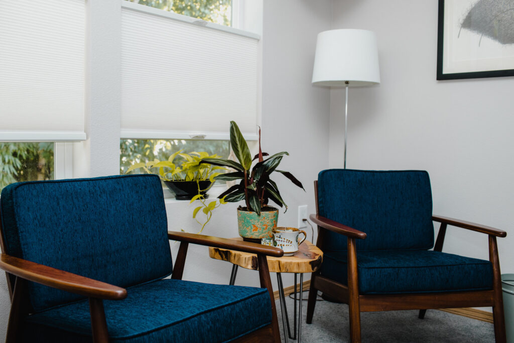 Photo of a cozy office with two empty armchairs, a lamp, and a wooden table with a potted plant.