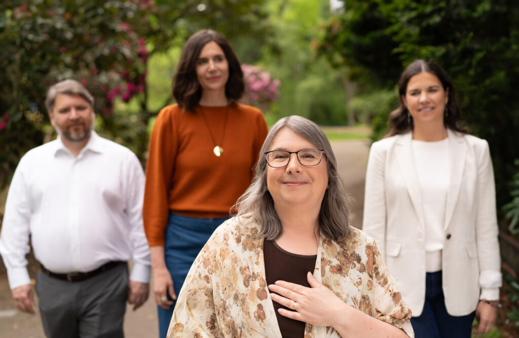 Photo of Linda, with hand on her heart, standing in front of the rest of the team.